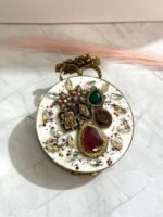 A gold clutch with jewel-toned gemstones, featuring a floral design and sparkling crystals, placed on a marble surface.