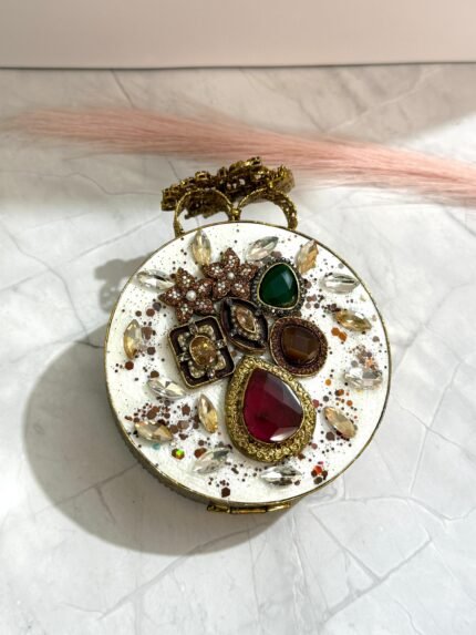 A gold clutch with jewel-toned gemstones, featuring a floral design and sparkling crystals, placed on a marble surface.
