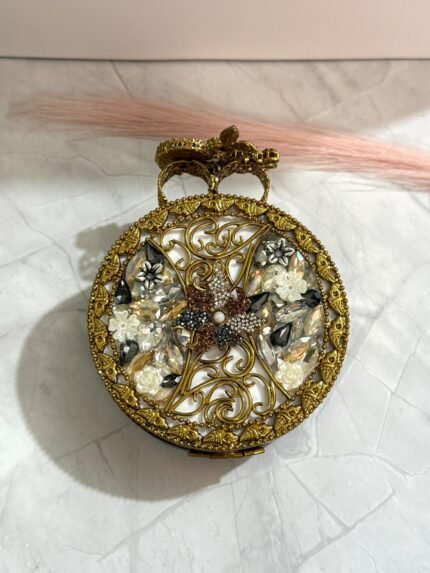 A gold clutch with jewel-toned gemstones, featuring a floral design and sparkling crystals, placed on a marble surface.