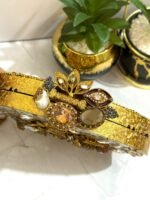 A gold and crystal embellished clutch with pearls, a rose accent, and a tassel detail, placed alongside decorative plants.