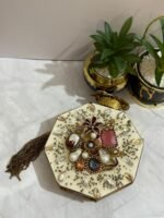 A luxurious octagonal clutch with gold accents, jewel-toned crystals, pearls, and a tassel detail, placed alongside decorative plants.
