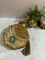 A luxurious octagonal clutch with gold accents, jewel-toned crystals, pearls, and a tassel detail, placed alongside decorative plants.