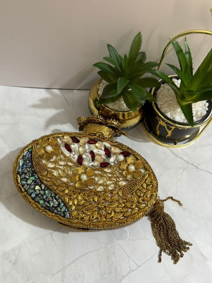 A luxurious oval clutch with green gemstones, pearls, and gold detailing, finished with a tassel, placed alongside decorative plants.