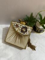 A square clutch with a green beaded floral design, crystal embellishments, and a tassel, placed next to decorative plants.