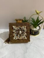 A gold clutch with a crystal and pearl flower embellishment, placed next to decorative plants, with a gold tassel attached.