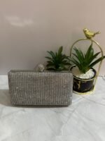 A silver crystal-embellished clutch with a sleek design, placed next to decorative plants.