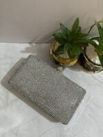 A silver crystal-embellished clutch with a sleek design, placed next to decorative plants.