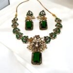 A green and gold necklace set with pearl and crystal embellishments, including matching earrings, displayed on a white surface.