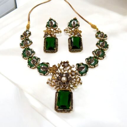 A green and gold necklace set with pearl and crystal embellishments, including matching earrings, displayed on a white surface.