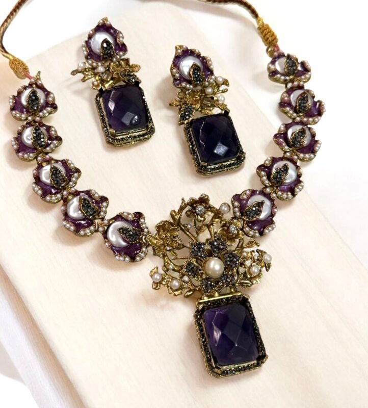 A luxurious amethyst and pearl necklace set with intricate gold detailing, including matching earrings, displayed on a light-colored background.