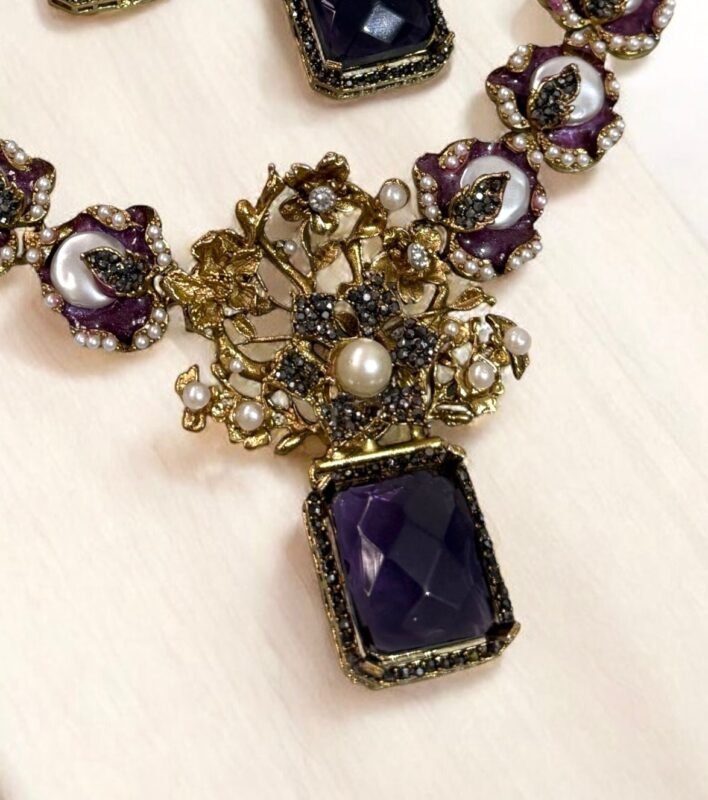 A luxurious amethyst and pearl necklace set with intricate gold detailing, including matching earrings, displayed on a light-colored background.