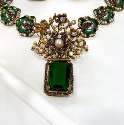 A green and gold necklace set with pearl and crystal embellishments, including matching earrings, displayed on a white surface.