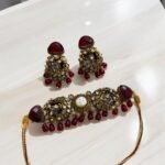 A red and gold necklace set with pearls and crystal detailing, including matching earrings, displayed on a light-colored background.