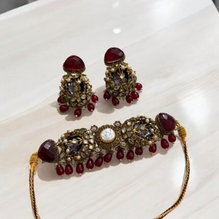 A red and gold necklace set with pearls and crystal detailing, including matching earrings, displayed on a light-colored background.