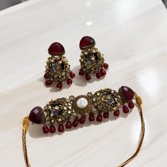 A red and gold necklace set with pearls and crystal detailing, including matching earrings, displayed on a light-colored background.