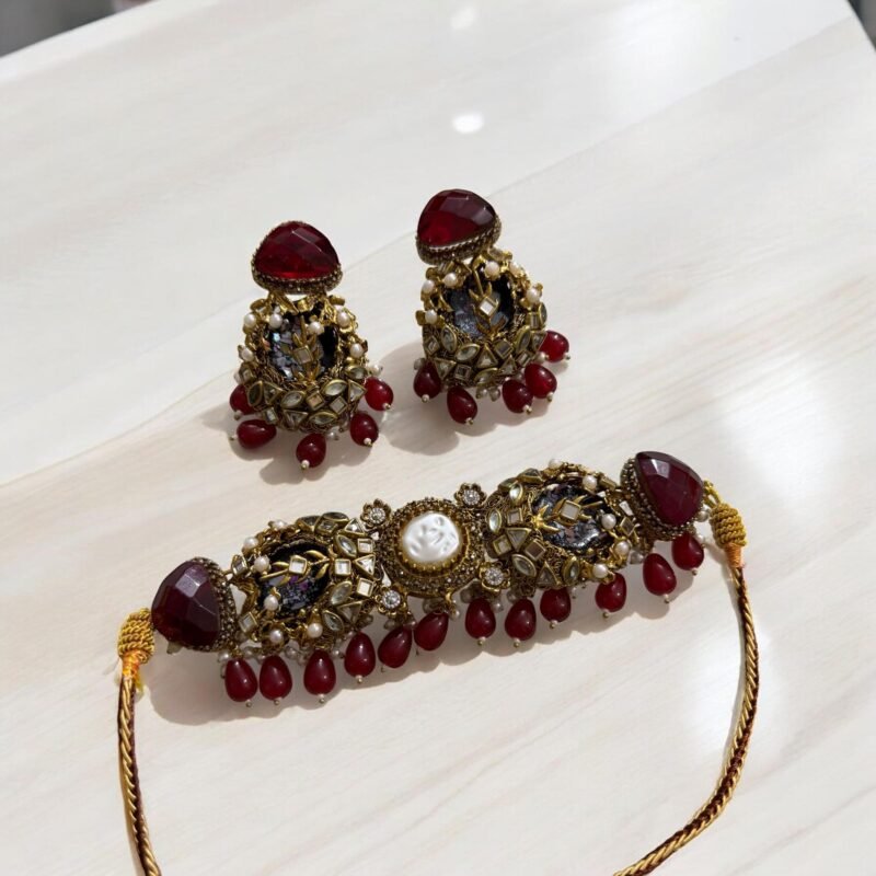 A red and gold necklace set with pearls and crystal detailing, including matching earrings, displayed on a light-colored background.
