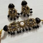 A black and gold necklace set with pearl and crystal detailing, including matching earrings, displayed on a light background.