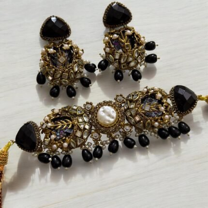 A black and gold necklace set with pearl and crystal detailing, including matching earrings, displayed on a light background.