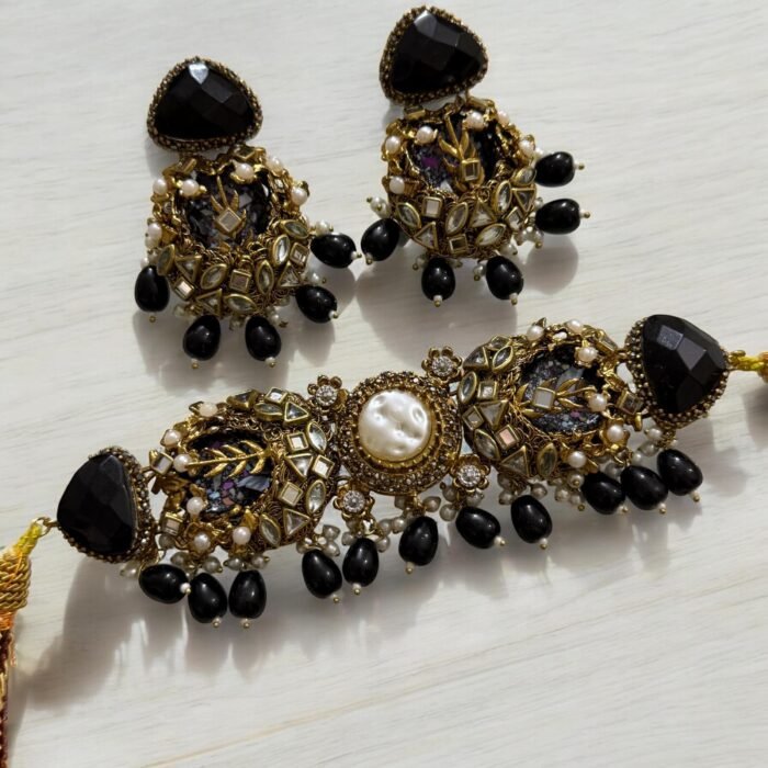 A black and gold necklace set with pearl and crystal detailing, including matching earrings, displayed on a light background.