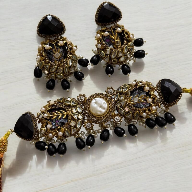 A black and gold necklace set with pearl and crystal detailing, including matching earrings, displayed on a light background.