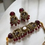 A red and gold necklace set with pearls and crystal detailing, including matching earrings, displayed on a light-colored background.