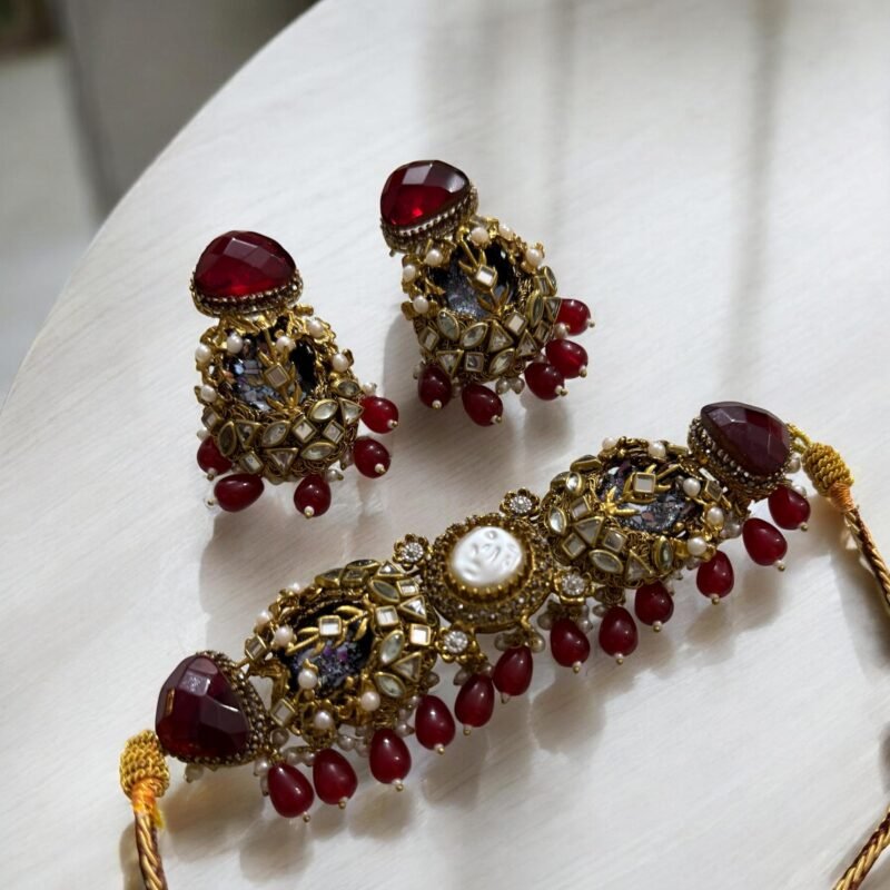 A red and gold necklace set with pearls and crystal detailing, including matching earrings, displayed on a light-colored background.