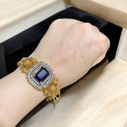 Gold bracelet with a sapphire stone centerpiece and crystal embellishments.