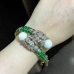 Gold bracelet with green stones, white pearls, and crystal embellishments.