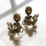 Gold earrings with peach gemstones, pearls, and crystal embellishments in a floral design.