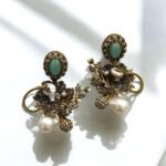 Gold earrings with peach gemstones, pearls, and crystal embellishments in a floral design.