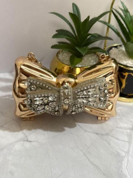 Gold bow-shaped clutch with crystal embellishments, featuring a detachable gold chain strap.