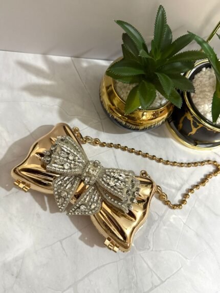 Gold bow-shaped clutch with crystal embellishments, featuring a detachable gold chain strap.
