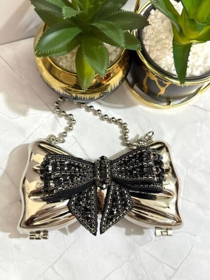 Silver clutch with black sequin bow design, featuring a detachable chain strap.