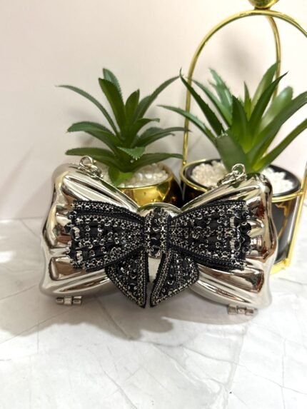 Silver clutch with black sequin bow design, featuring a detachable chain strap.