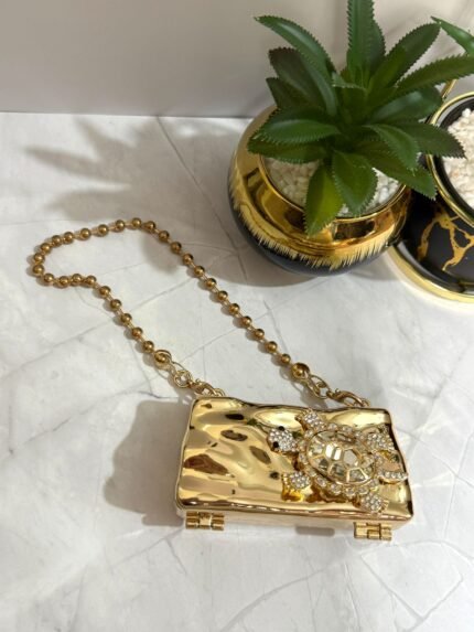 Gold clutch with a crystal turtle design, featuring a detachable gold chain strap.