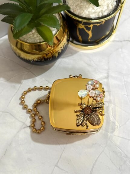 Gold clutch with a bee and floral crystal design, featuring a detachable gold chain strap.