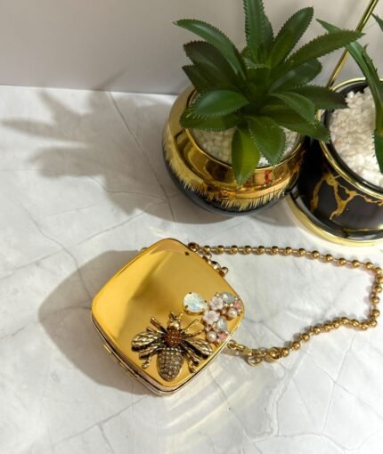 Gold clutch with a bee and floral crystal design, featuring a detachable gold chain strap.