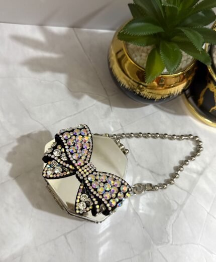Silver clutch with a black and crystal bow design, featuring a detachable silver chain strap.